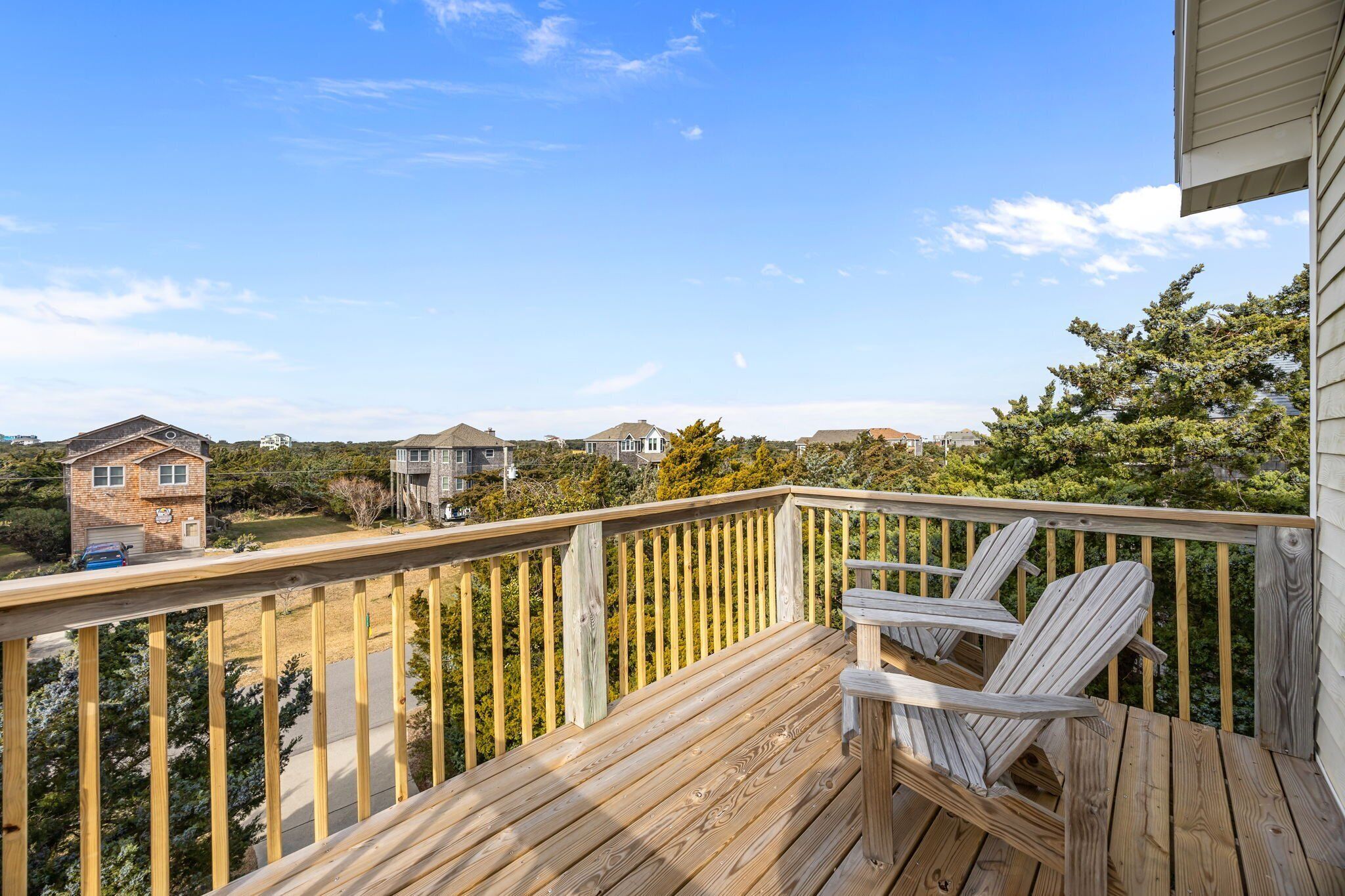 A wooden deck with two Adirondack chairs, overlooking a residential area with houses and trees.