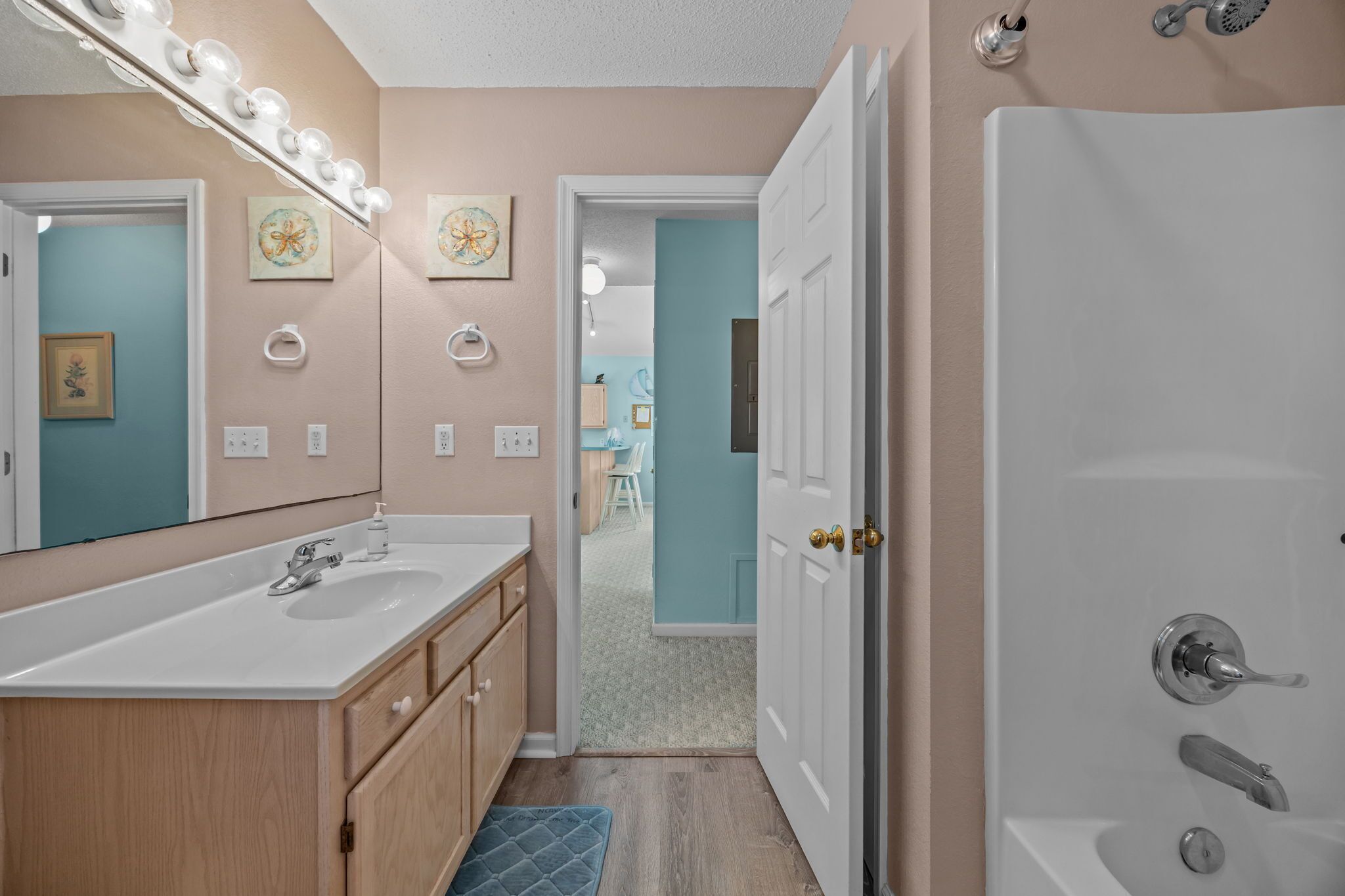 Une salle de bain avec un meuble-lavabo, un évier et un miroir. Il y a des luminaires au-dessus du miroir et une douche avec une porte.