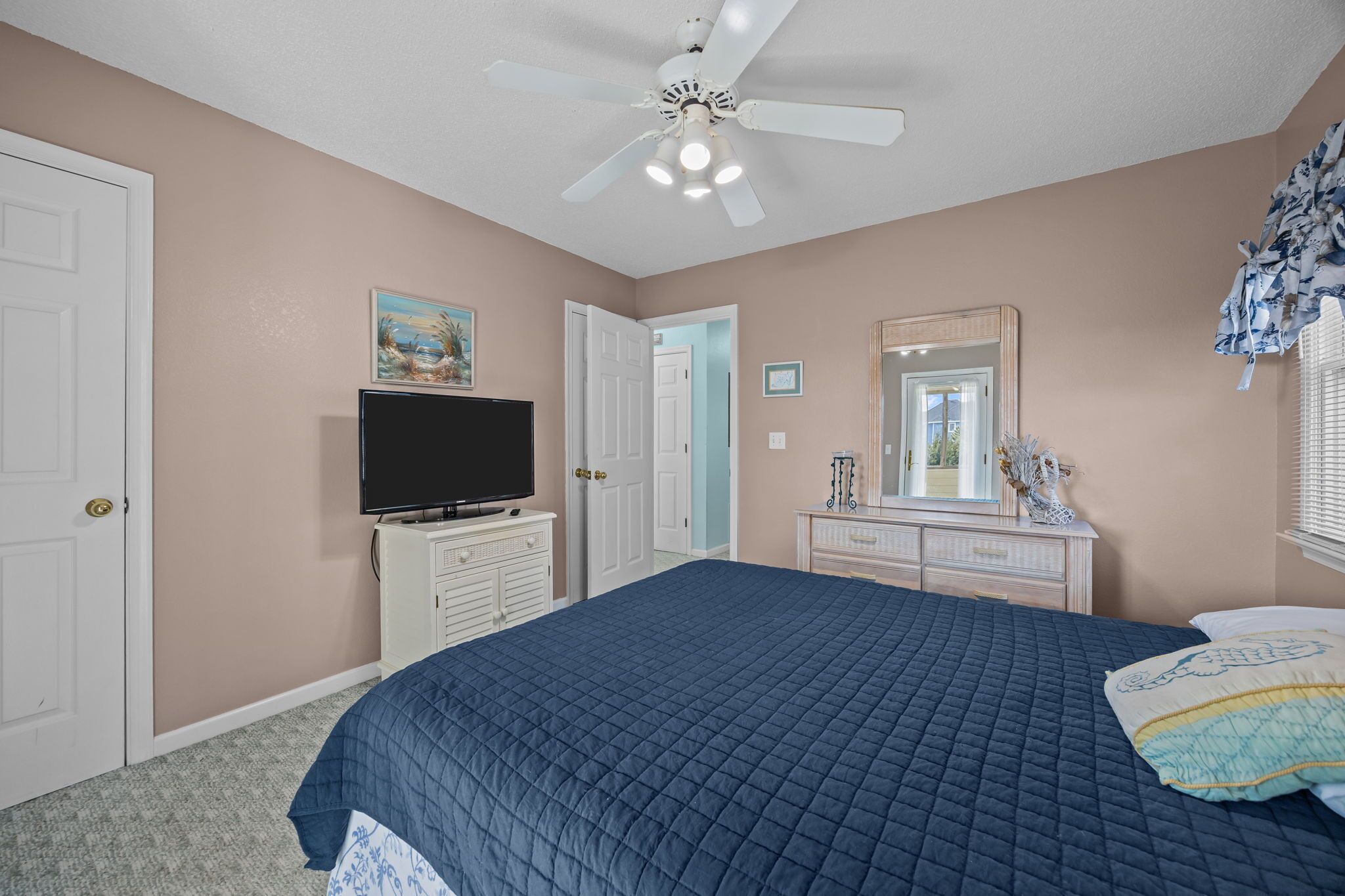 A bedroom with a bed, a television, a dresser, a mirror, and a ceiling fan.