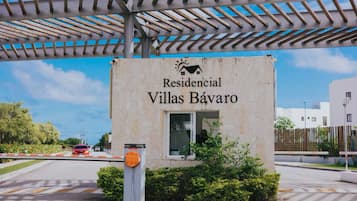 Une enseigne indiquant « Residencial Villas Bávaro », avec une vue dégagée sur l’entrée et une allée menant à un portail.