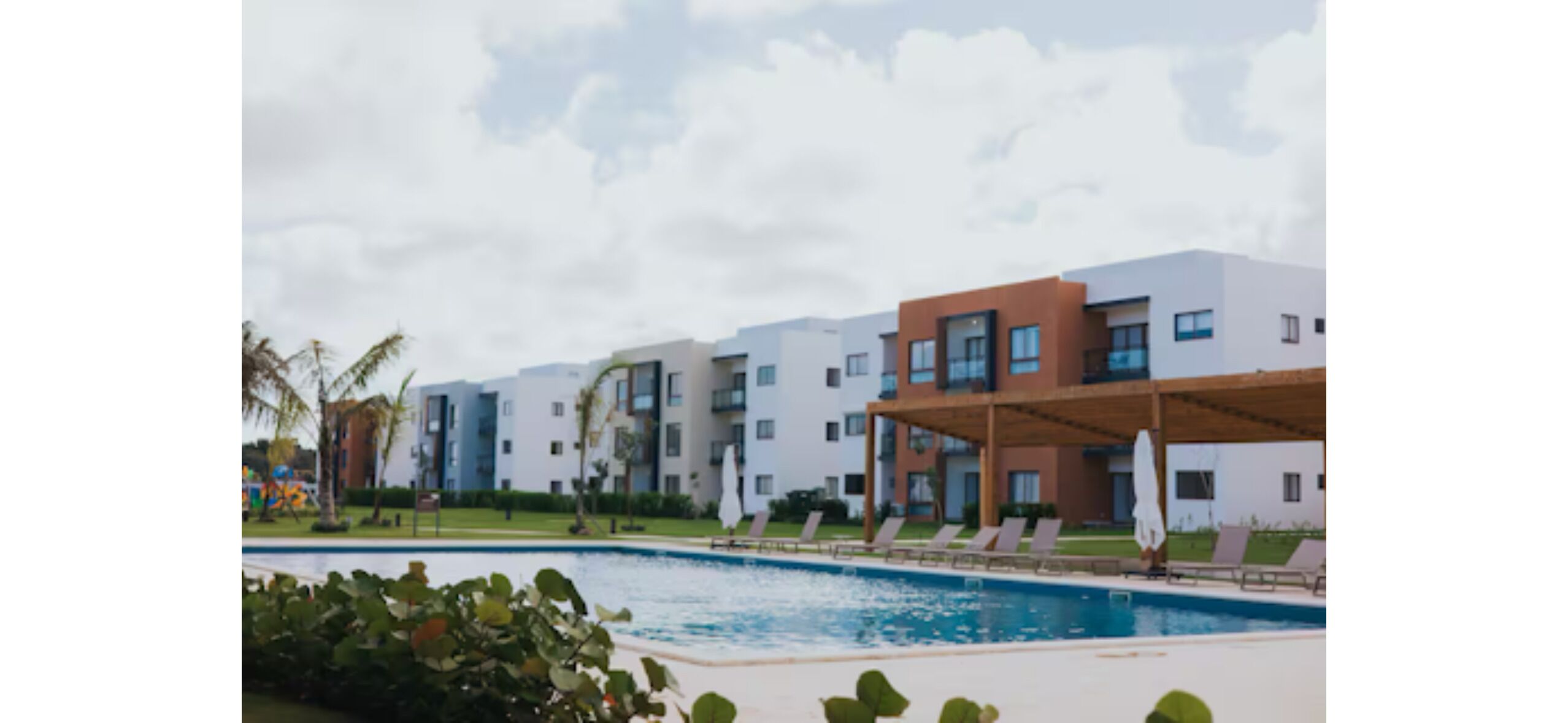 Ein modernes Hotel mit Schwimmbad, mehreren Balkonen und einer überdachten Außenbereich mit Liegestühlen.