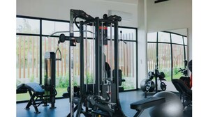 Une salle de sport équipée de divers appareils d’exercice, dotée de grandes fenêtres et offrant une vue sur la verdure environnante.
