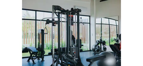 Et fitnesscenter med forskellig træningsudstyr, store vinduer og udsigt til grøn natur udefra.