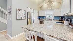 Una cocina moderna con encimeras de granito, armarios blancos, un refrigerador de acero inoxidable y un reloj en la pared.