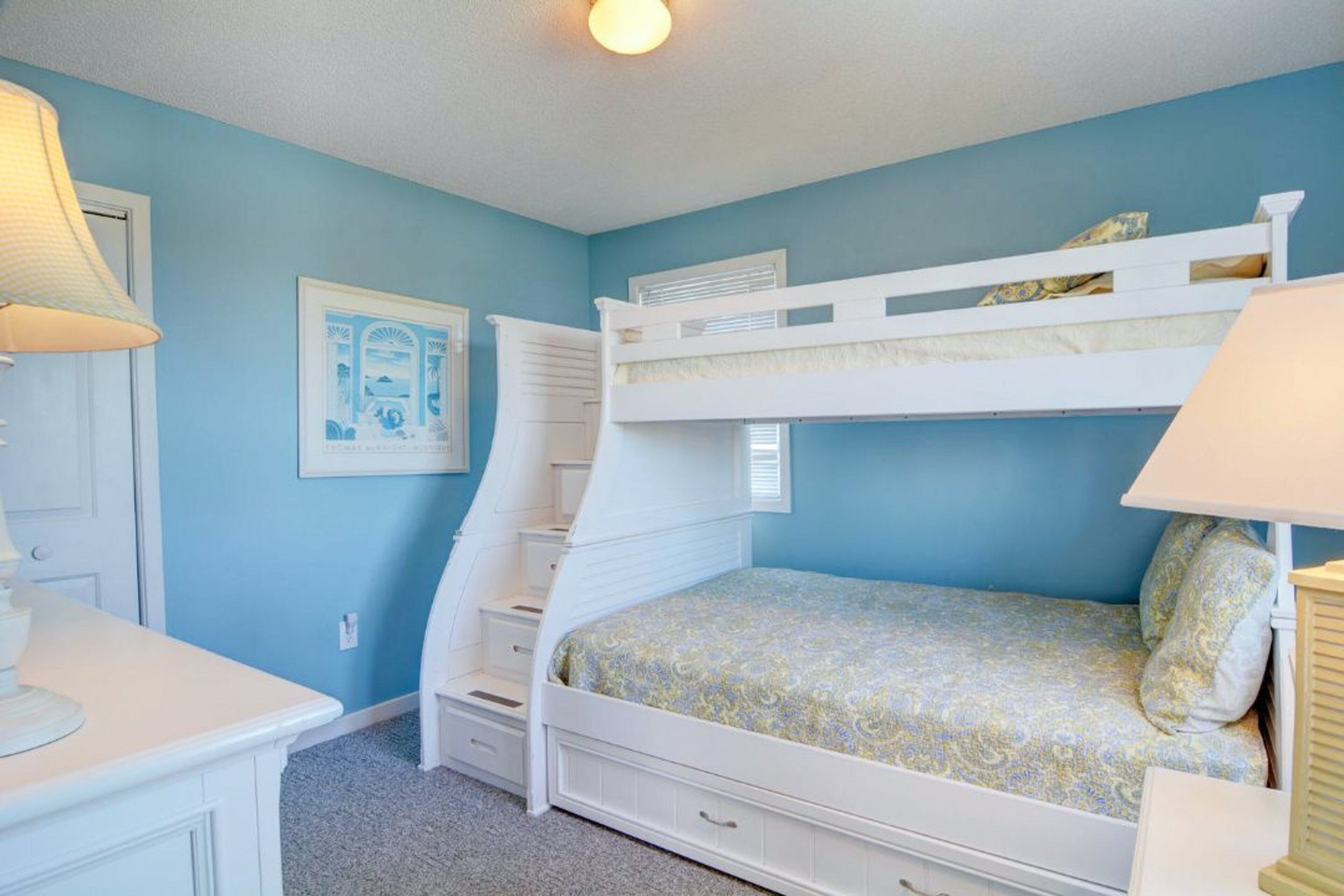Een slaapkamer met een stapelbed, een blauwe muur, een wit bureau en een lijst aan de muur.