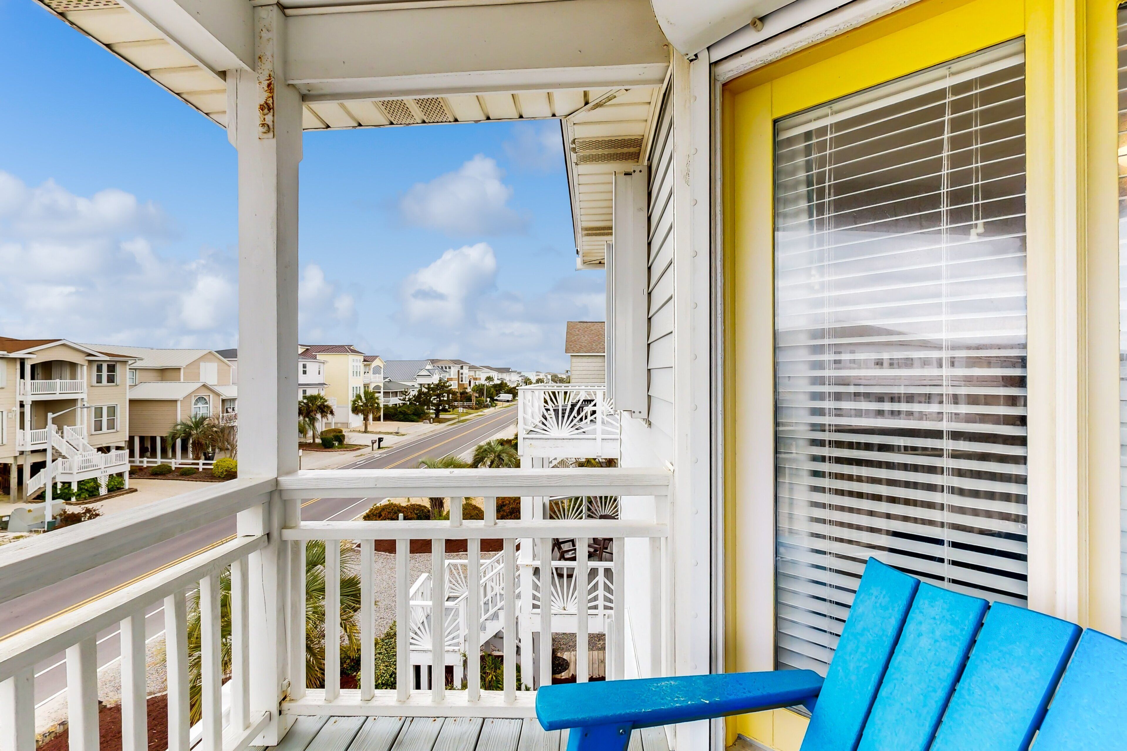 Un balcón con vista a una calle residencial, un banco azul y una ventana con persianas.