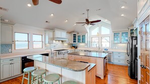 A spacious kitchen with a large island, bar stools, and a ceiling fan. - Waterfront home with amazing sound view, private pool, hot tub, & game room (Avon)