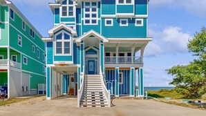 A two-story beachfront house with a balcony, a front porch, and a staircase leading to the entrance. - Waterfront home with amazing sound view, private pool, hot tub, & game room (Avon)
