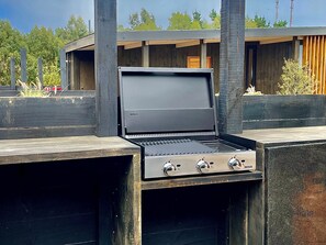 An outdoor grill with a digital display, set against a wooden structure with a view of trees and a building in the background. - Chackra Centinela  (Navidad)