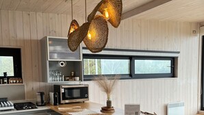 A modern kitchen with wooden cabinets, a microwave, and a coffee maker. There are woven light fixtures, a vase with dried plants, and a welcome sign on the counter. - Chackra Centinela  (Navidad)