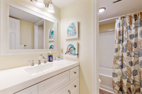 A bathroom with a white sink, two faucets, a mirror, and a shower curtain with a sea shell pattern.