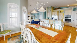 A spacious dining area with a wooden table, white chairs, and a chandelier. - Grams Getaway: Private pool, deck, & patio - walk to the beach (Ocean Isle Beach)