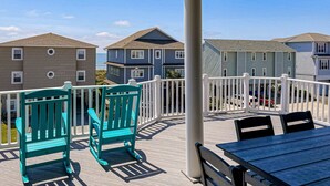 A wooden deck with teal chairs and a table, overlooking a residential area with houses and a clear sky. - Grams Getaway: Private pool, deck, & patio - walk to the beach (Ocean Isle Beach)