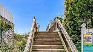 A wooden staircase leading to a beach area with a signboard displaying beach rules and QR code. - Grams Getaway: Private pool, deck, & patio - walk to the beach (Ocean Isle Beach)