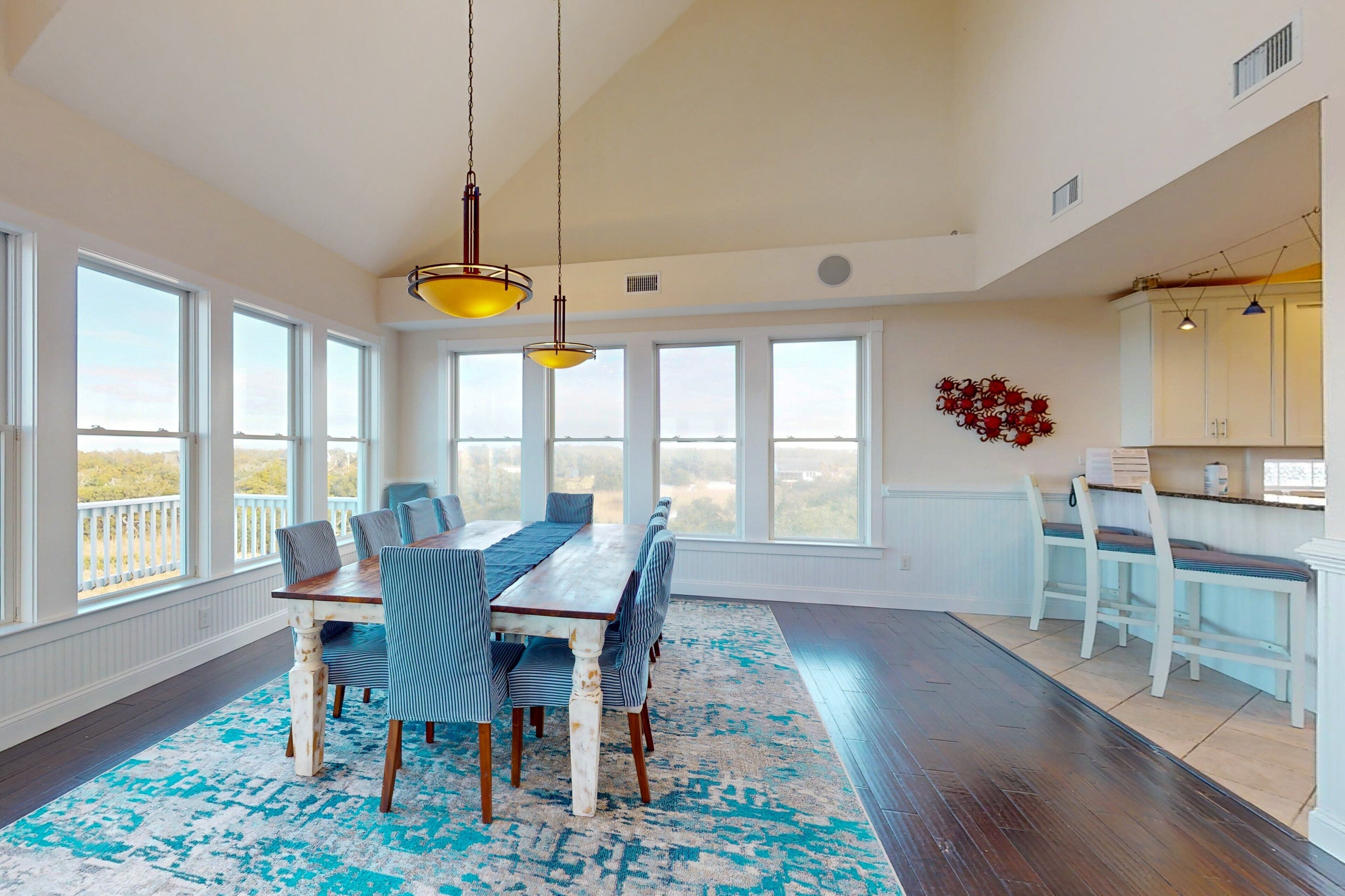 A spacious dining area with a long table and chairs, large windows, and a view of the outdoors.