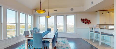 A spacious dining area with a long table and chairs, large windows, and a view of the outdoors.