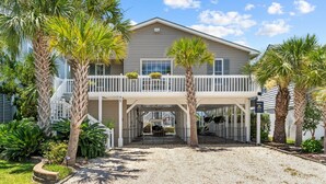 A two-story house with a covered porch, palm trees, and a gravel driveway. - Fore Buoys: Canalfront, dock, close to beach! (Ocean Isle Beach)