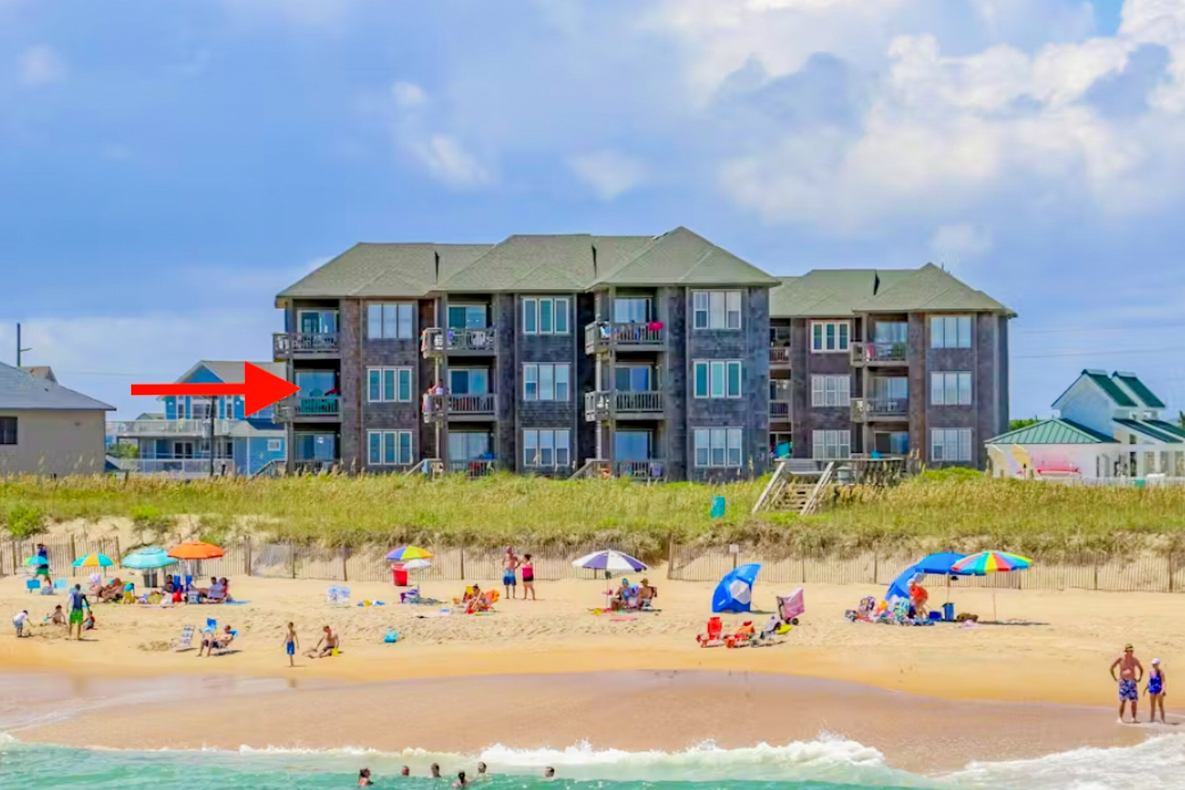 Un hôtel situé en bord de mer, doté de nombreux balcons, de parasols et d’une plage de sable.