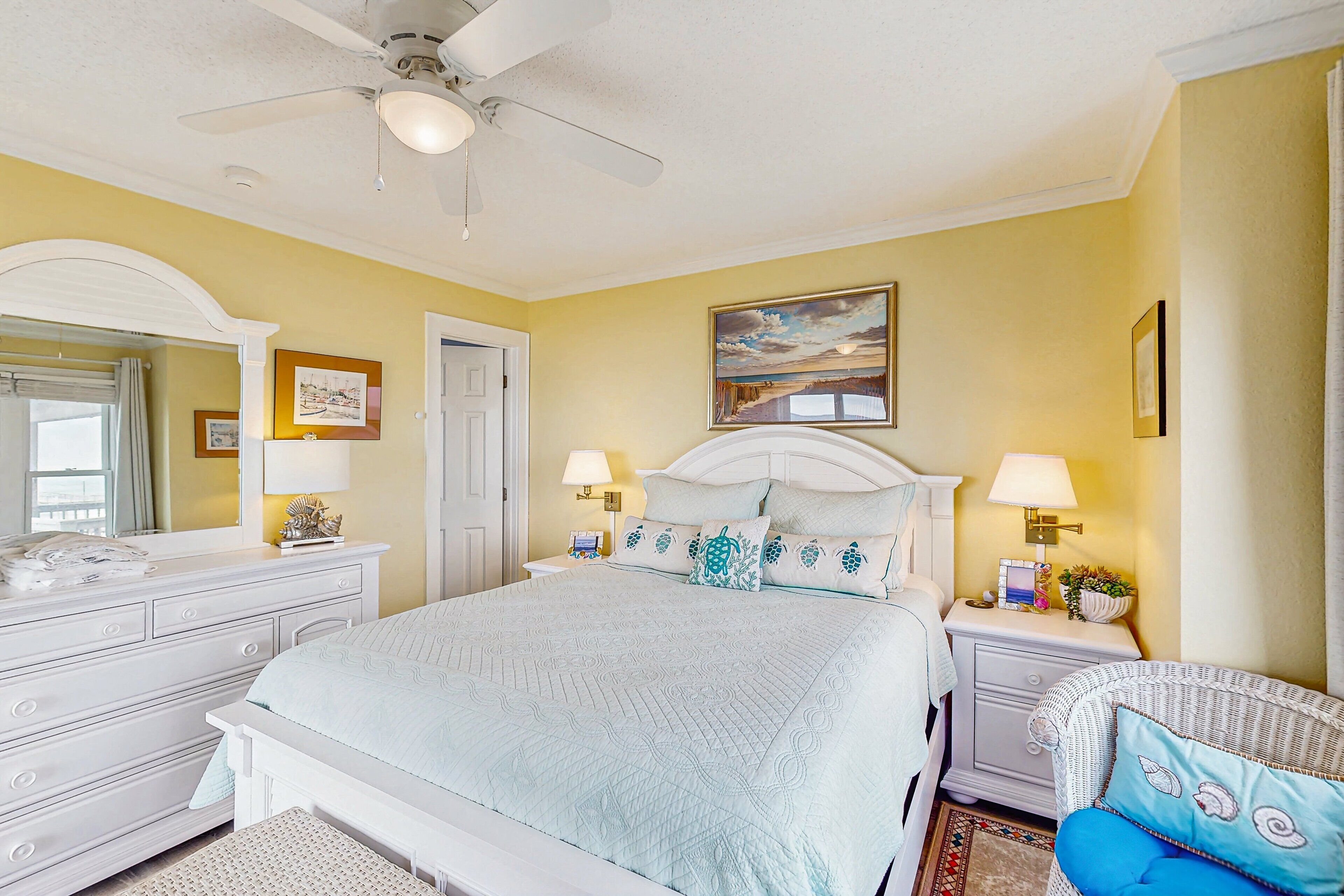 A bedroom with a bed, nightstands, a chair, a ceiling fan, and a painting on the wall.