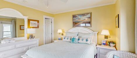 A bedroom with a bed, nightstands, a chair, a ceiling fan, and a painting on the wall.