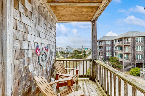 A wooden deck with two Adirondack chairs, a ship's wheel, and American flags.