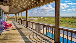 A wooden deck with a pool, red chairs, and a view of the beach. - Dog-friendly oceanfront home with private outdoor pool, hot tub & central AC (Waves)