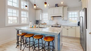 A spacious kitchen with a large island, bar stools, and a stainless steel refrigerator. - Dog-friendly oceanfront home with private outdoor pool, hot tub & central AC (Waves)