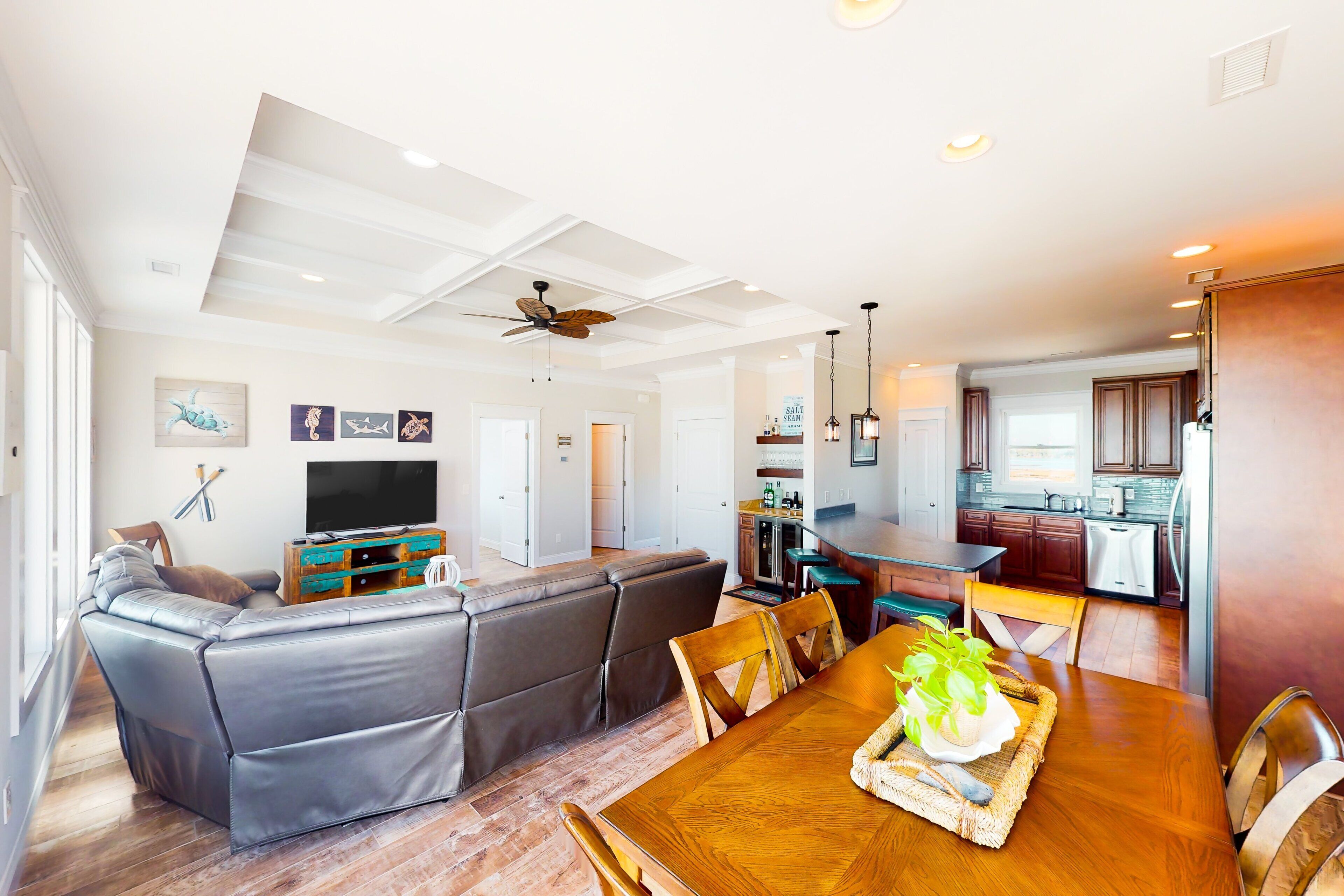 A modern living room with a sectional sofa, a wooden dining table with a tray, and a kitchen in the background.