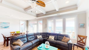 A living room with a large sectional sofa, a wooden coffee table, and a ceiling fan. - Beautiful dog-friendly ocean view home with hot tub, lovely balcony, W/D & AC (North Topsail Beach)