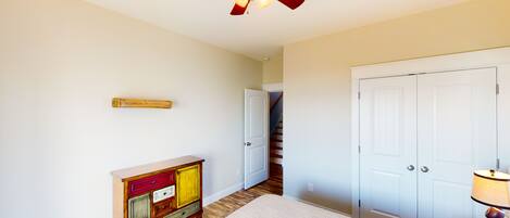 A bedroom with a bed, a ceiling fan, a dresser, a door, and a lamp.