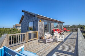 A wooden deck with red lounge chairs and a small building with large windows.