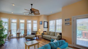 A spacious living room with a large window, a ceiling fan, and a sofa. - Ocean View Duplex in Hampton Colony - Community Pool & Just Steps to the Beach!! (North Topsail Beach)