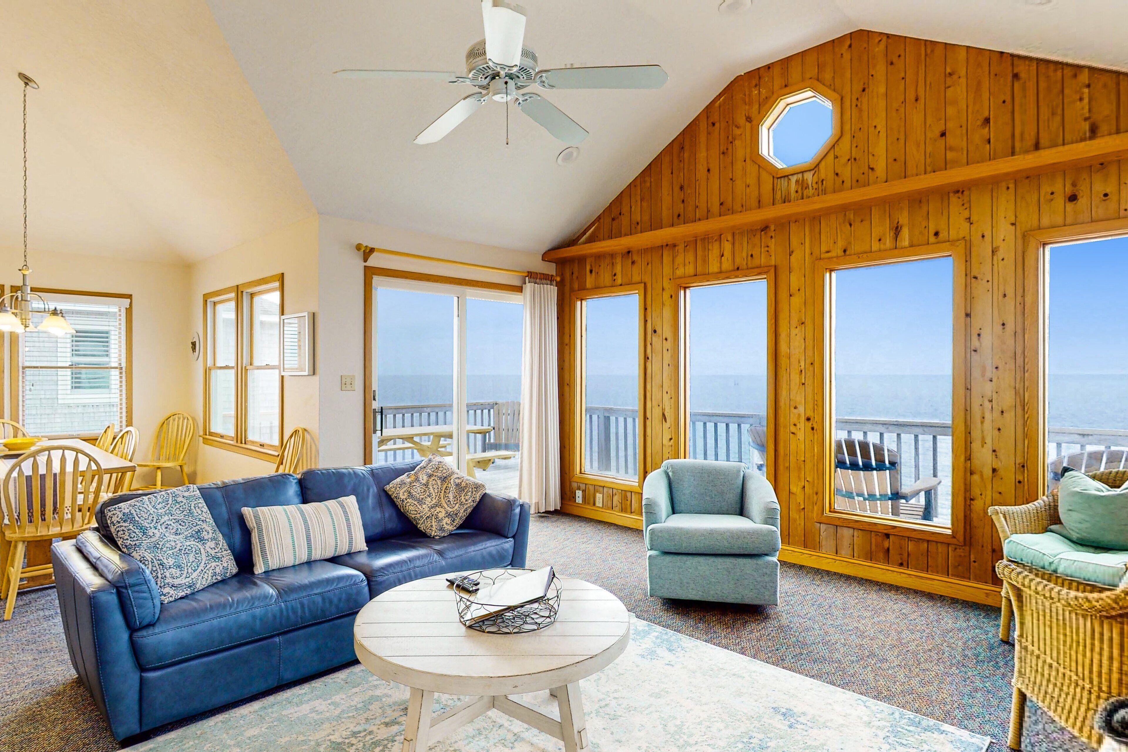 A spacious living room with a blue sofa, a round coffee table, and a view of the ocean through large windows.