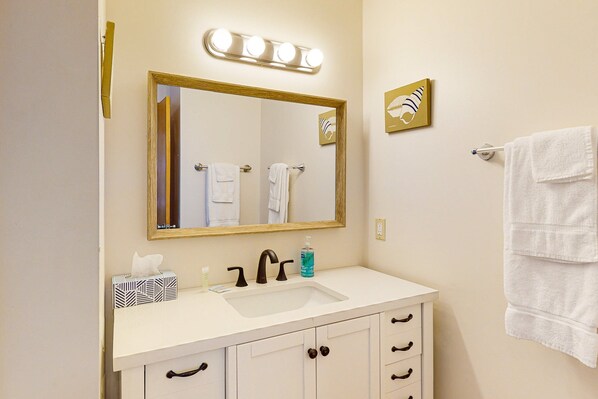 Un baño con tocador blanco, un espejo grande con iluminación y un perchero para toallas.