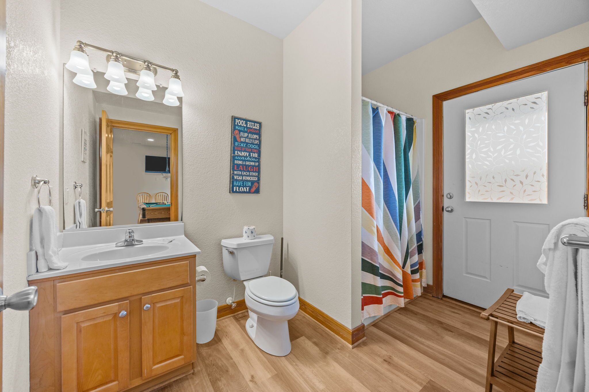 Un bagno con un mobile lavabo in legno, un water bianco, uno specchio con illuminazione e una tenda da doccia colorata a righe.