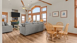 Ein geräumiges Wohnzimmer mit grauem Sofa, Holzesstisch mit Stühlen und Deckenventilator.
