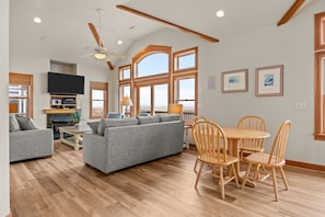 A spacious living room with a gray sofa, wooden dining table with chairs, and a ceiling fan. - Oceanfront home with private pool, hot tub, game room, sundecks & fast WiFi (Waves)