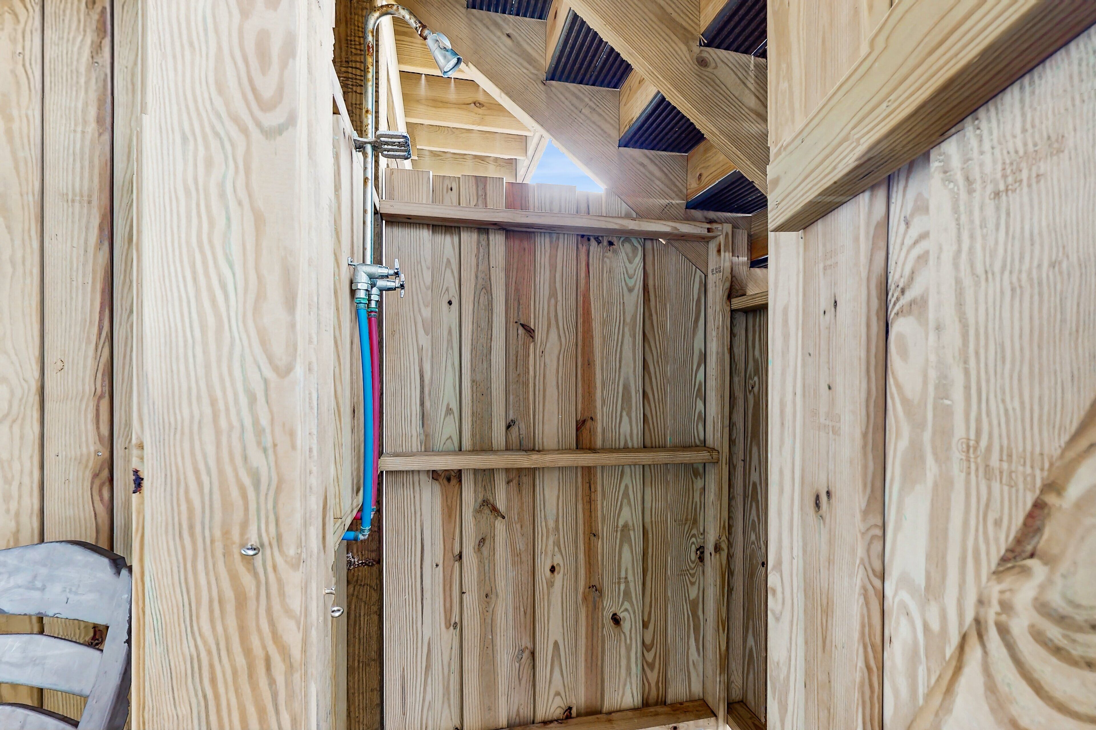 A wooden interior with a visible shower area, a metal pipe, and a wooden ceiling structure.