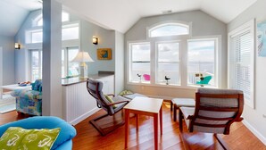 Una habitación luminosa y espaciosa con techo alto, ventanas grandes y una zona de estar acogedora con mesa y sillas.