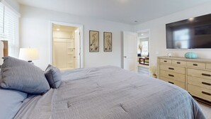 Une chambre à coucher comprenant un grand lit, une commode, un téléviseur à écran plat et deux œuvres d’art accrochées au mur.