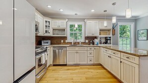 A modern kitchen with white cabinetry, stainless steel appliances, and a wooden floor.