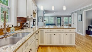 A spacious kitchen with granite countertops, white cabinetry, and a large island. There are stainless steel sinks and a coffee maker on the counter.