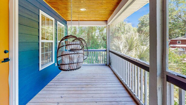 A wooden deck with a hanging chair, a railing, and a view of greenery.