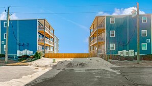 A modern apartment building with multiple balconies and a sandy area in front. - Cheerful beachfront condo with balcony, tennis court, & W/D - snowbird-friendly (North Topsail Beach)