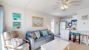 A living room with a sofa, armchair, and coffee table. There is a kitchen area with a refrigerator, microwave, and sink. - Cheerful beachfront condo with balcony, tennis court, & W/D - snowbird-friendly (North Topsail Beach)