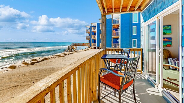 A wooden deck with a table and chairs, overlooking the ocean. - Cheerful beachfront condo with balcony, tennis court, & W/D - snowbird-friendly (North Topsail Beach)