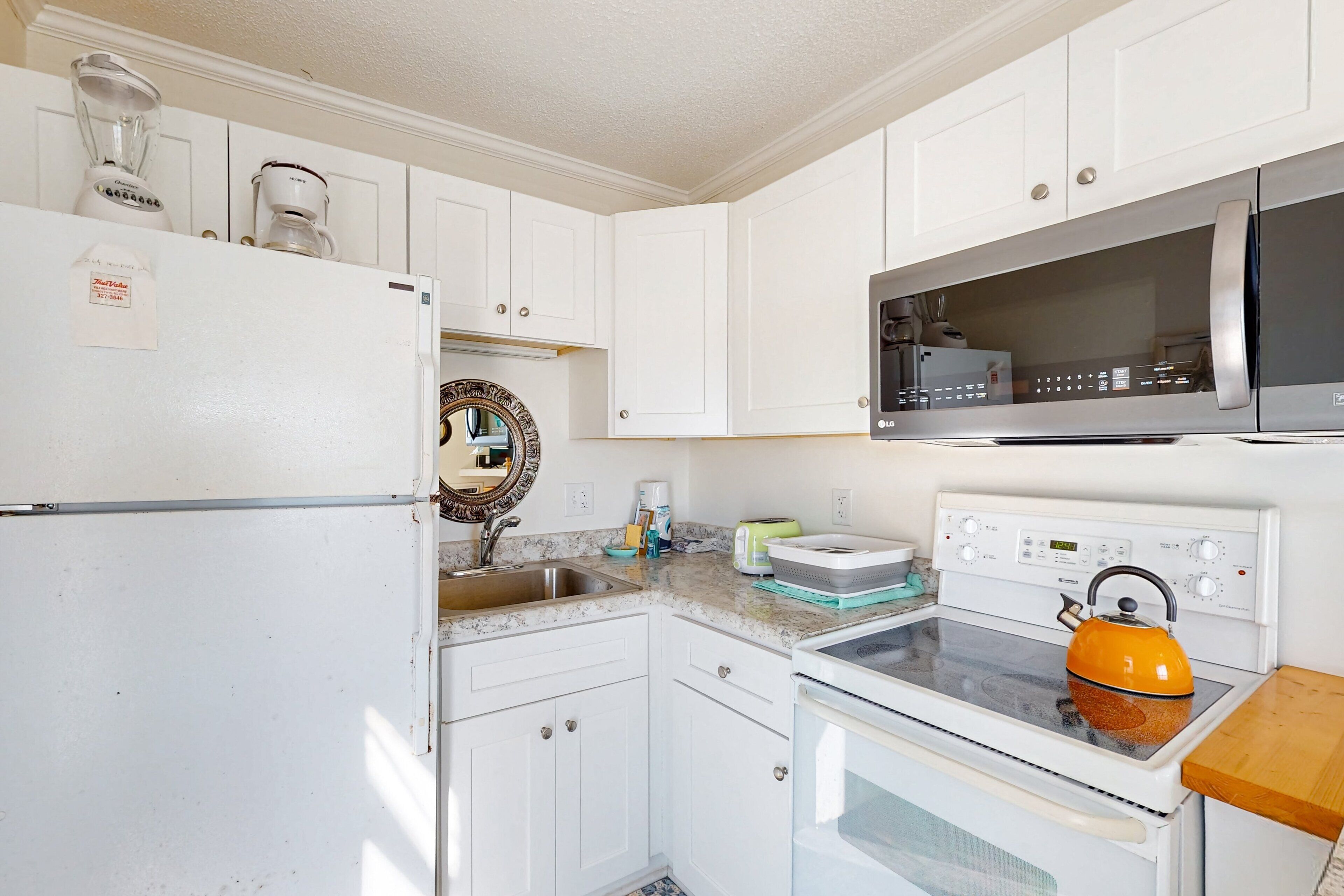 A kitchen with white cabinets, a refrigerator, a microwave, an oven, and a kettle.