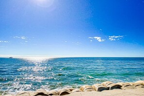 A beach with clear blue water, a boat in the distance, and a row of beige sea defenses in the foreground. - Cheerful beachfront condo with balcony, tennis court, & W/D - snowbird-friendly (North Topsail Beach)