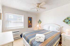 A bedroom with a bed, a ceiling fan, a window with blinds, a heater, and a nightstand with a lamp. - Cheerful beachfront condo with balcony, tennis court, & W/D - snowbird-friendly (North Topsail Beach)