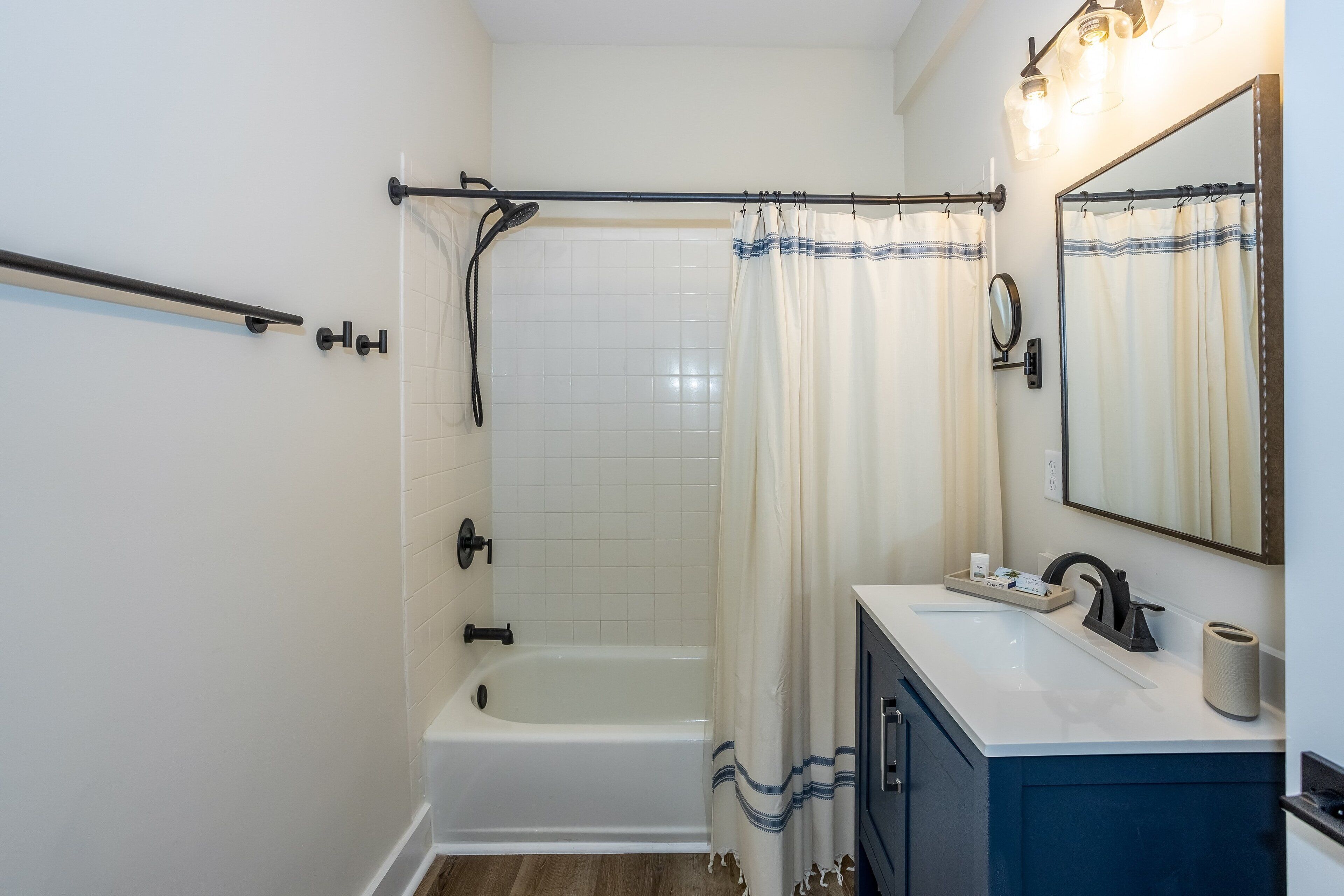 A bathroom with a bathtub, a shower curtain, a sink with a mirror, and a towel rack.
